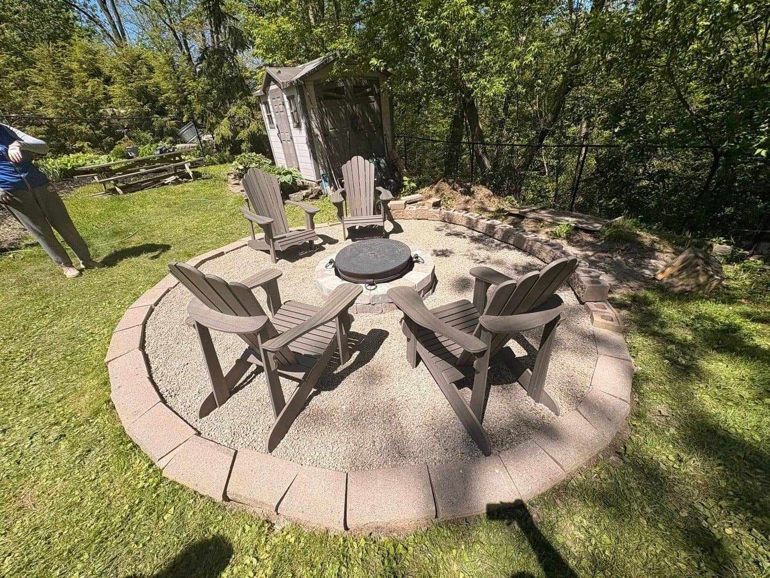 Stone fire pit with Adirondack chairs on a gravel patio
